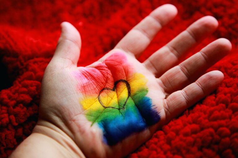 LGBTQ+ rainbow on a white hand, with a heart in the middle on a red fluffy background - illustration genital autonomy for transgender