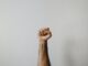 fist raised in the air on grey background, illutrating the need for help for intaction.org call for help stop profit from circumcision