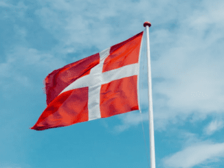 Danish flag white cross on a red background on a flag pole with a blue cloudy sky illustrating the article on 15square.org.uk about the debabte on male circumcision