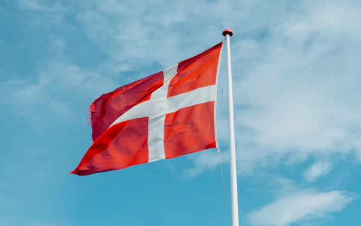 Danish flag white cross on a red background on a flag pole with a blue cloudy sky illustrating the article on 15square.org.uk about the debabte on male circumcision