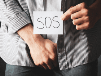 man holding a paper that says SOS and holding his grion- illusrating foreskin restoation survey article adressing the hidden trauma, also for smegma