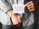 man holding a paper that says SOS and holding his grion- illusrating foreskin restoation survey article adressing the hidden trauma, also for smegma